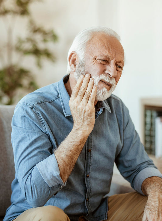 Older man holding his cheek and wincing in discomfort, illustrating tooth pain or dental sensitivity.