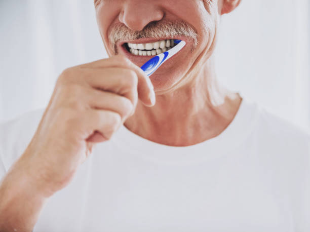 Man brushing his teeth with a blue toothbrush against a white background